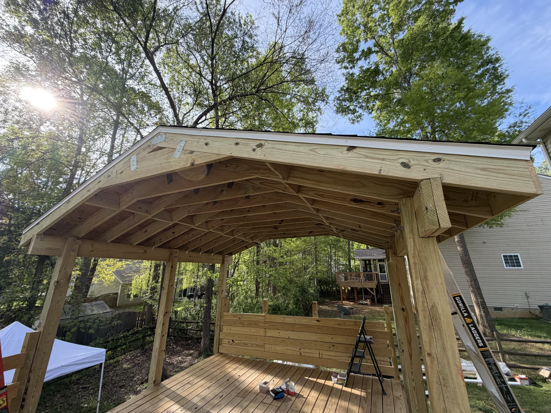 A timber pergola takes shape above a backyard deck. The photographs show the open roof framing, posts and connections during installation, before final finishing.