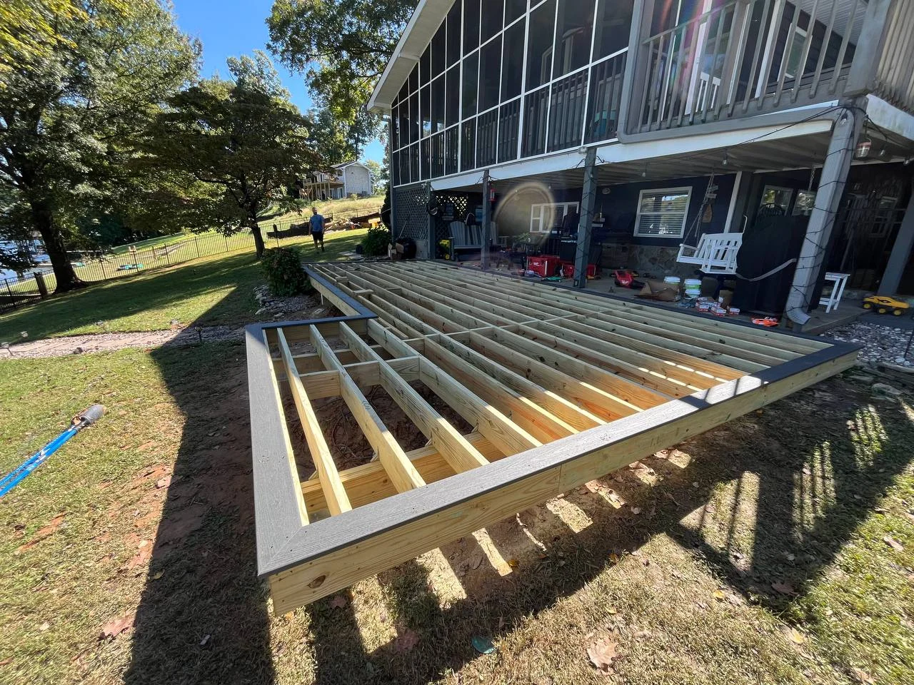 A deck construction journal beside an existing screened porch. These progress photographs show the timber framing, supporting posts and work area as the new outdoor platform takes shape.