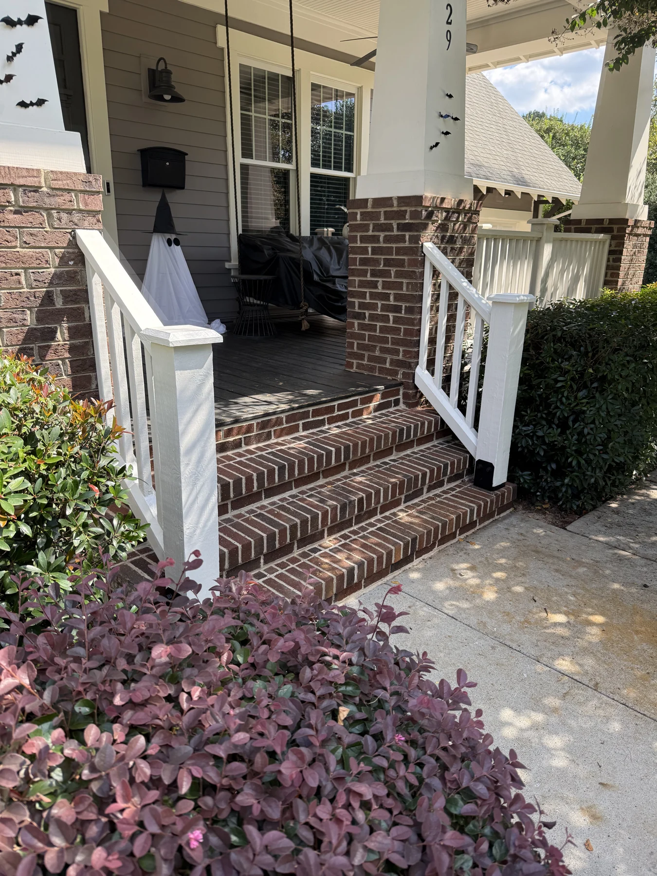 White entry posts and railings frame the brick steps at the home&rsquo;s entrance. Overall and close views show the porch approach and the junction between the post and masonry.
