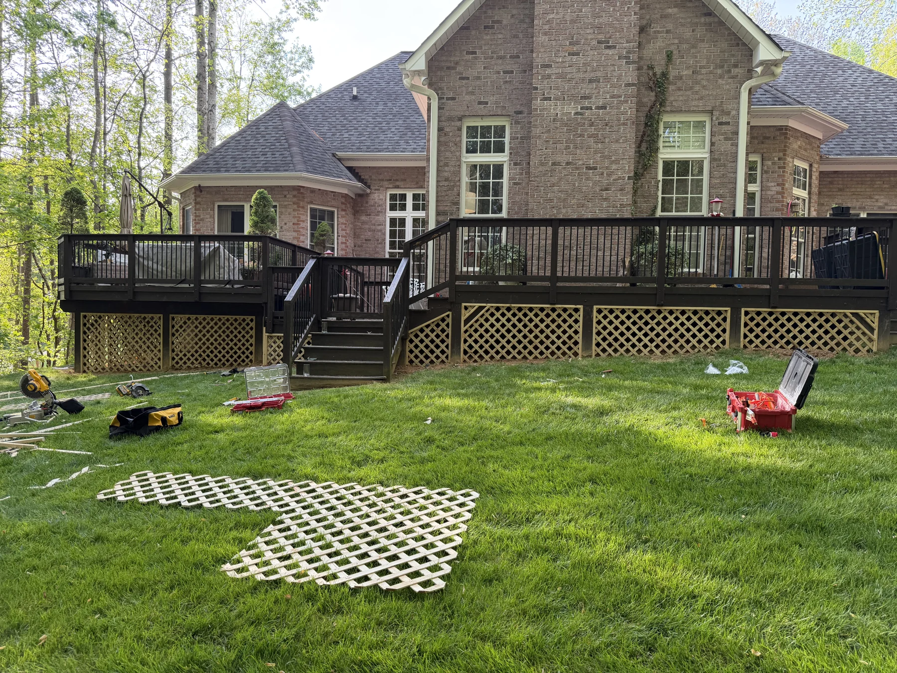 A backyard deck connects a brick home to its lawn, with dark railings, broad steps and space beside the covered porch. Daytime and evening photographs show the deck&rsquo;s connection to the house.