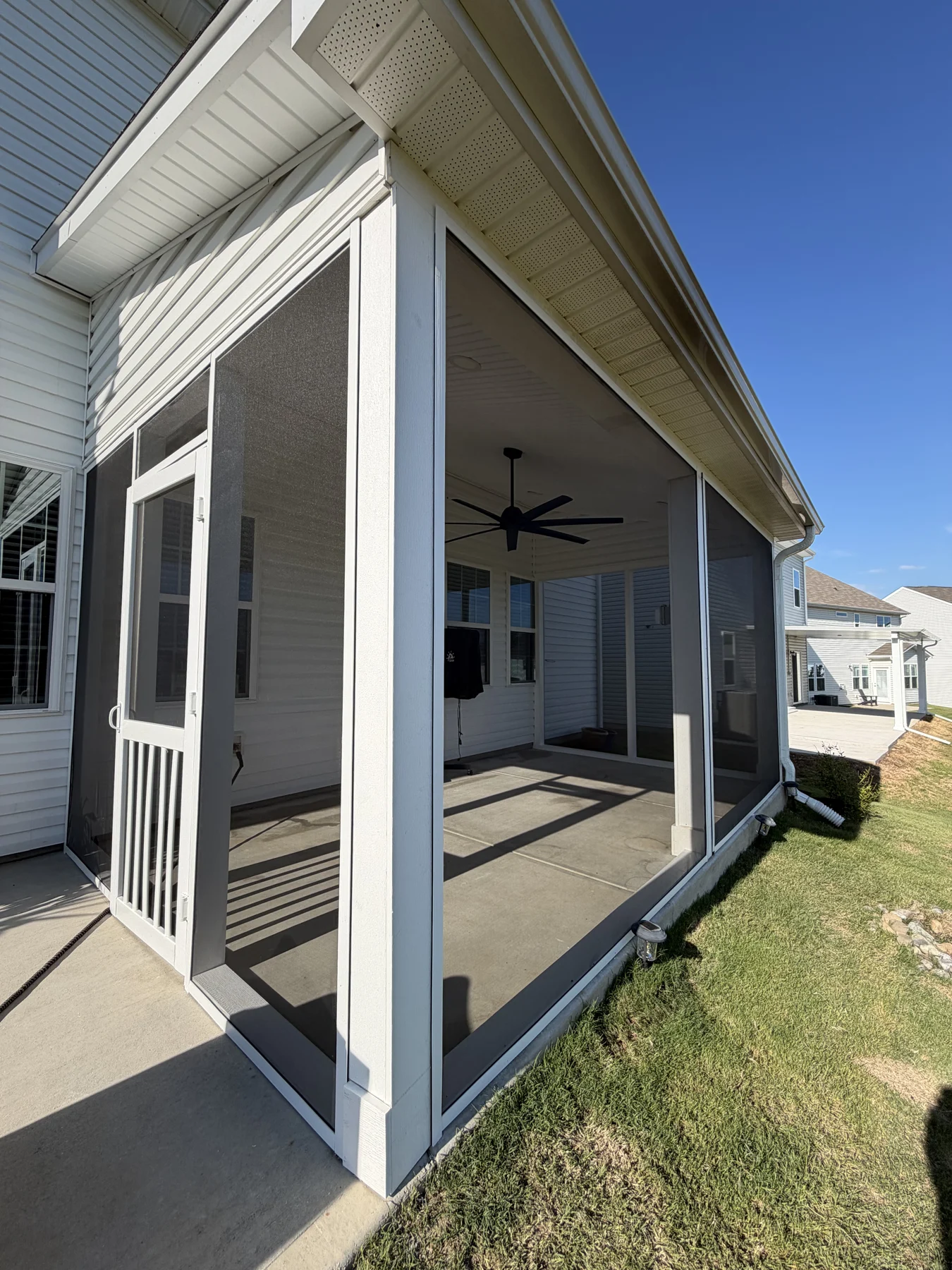 A covered patio extends the home&rsquo;s sheltered outdoor area toward the yard. White columns, a finished ceiling and a ceiling fan define an open space for gathering.