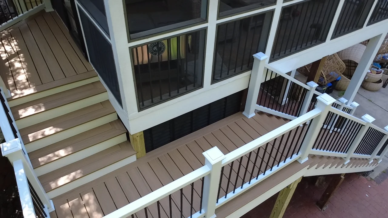 An elevated deck and staircase connect to a screened porch. Coordinated white posts, contrasting balusters and wood-toned walking surfaces carry the finish around the outdoor layout.