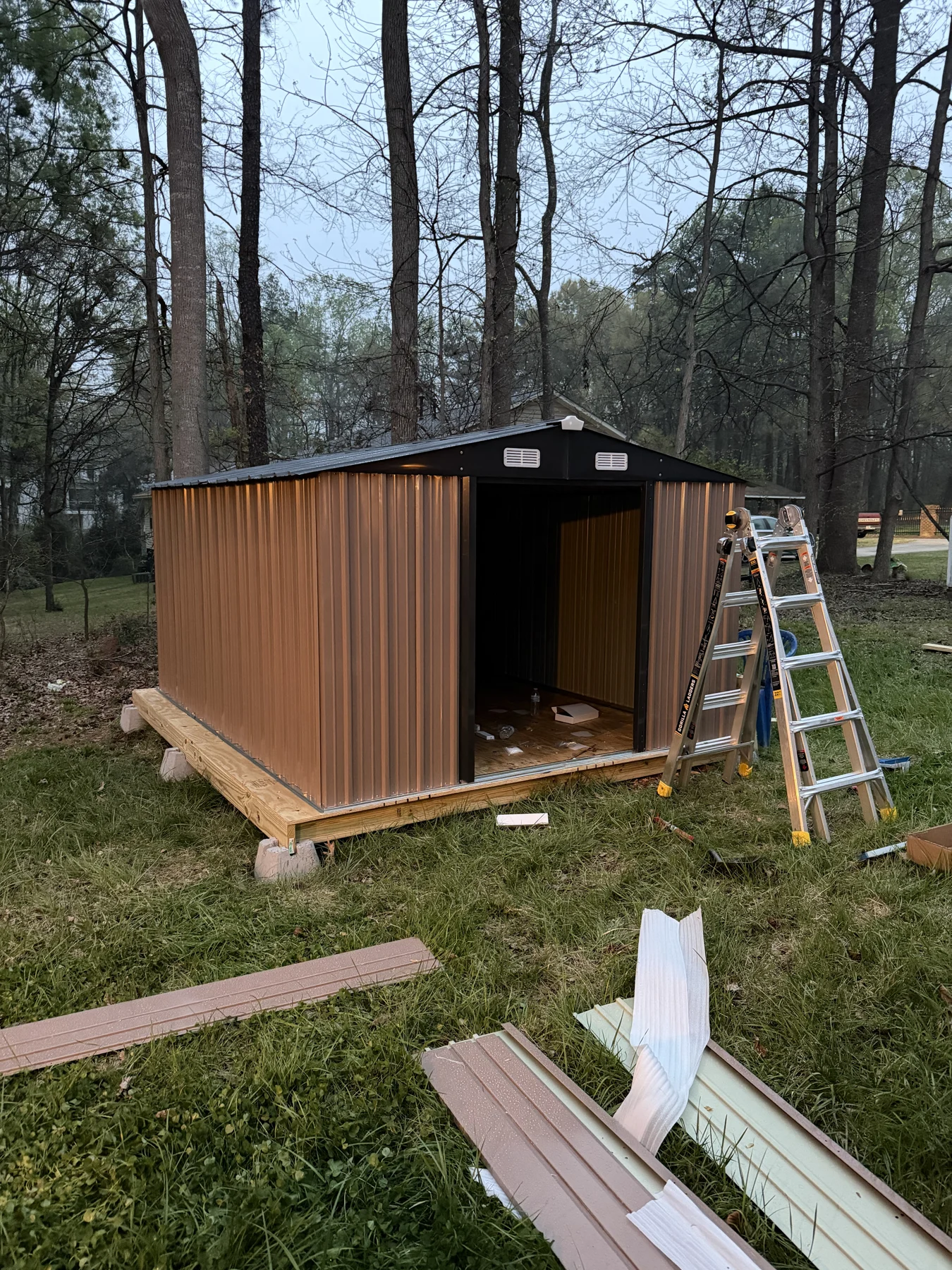 A compact backyard storage structure with timber siding and a wide entrance. This progress photograph records the exterior and entry while work is under way.