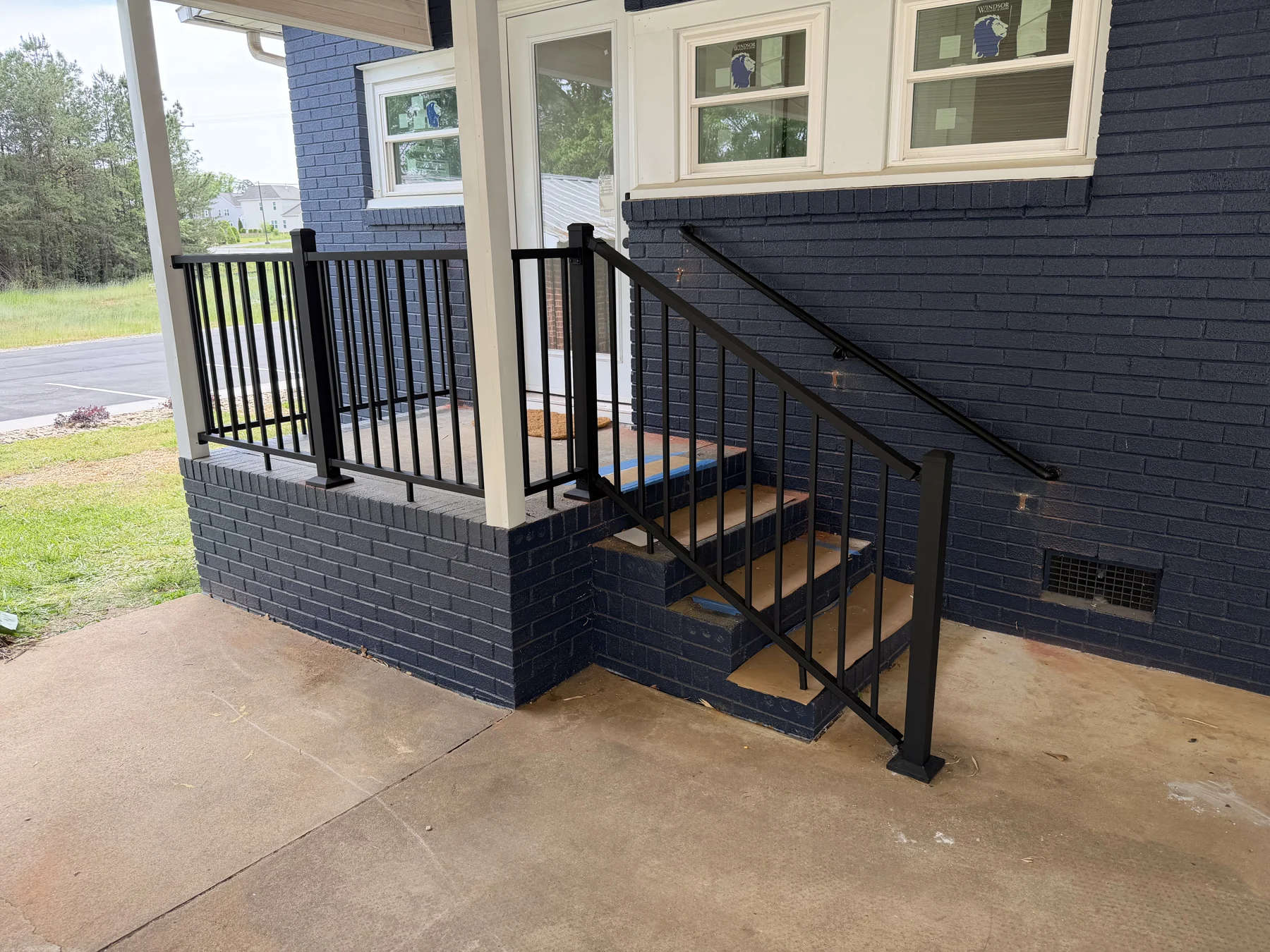 Dark railings and coordinated access steps define the covered porch and outdoor landing. The photographs show the porch from the approach, the walking surface and the rail details alongside the home.