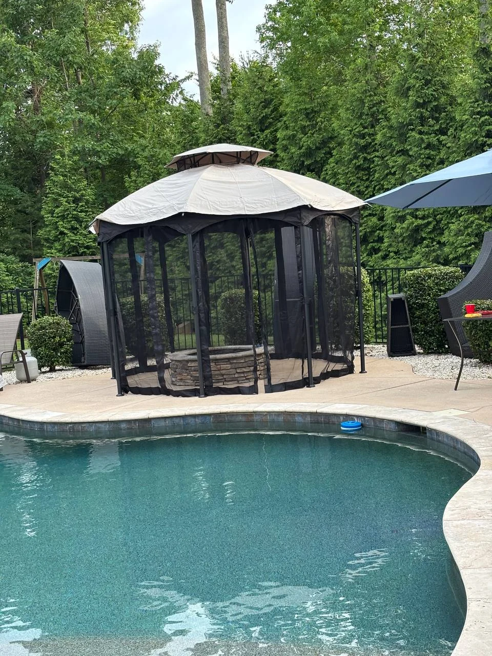 A freestanding screened gazebo sits beside a backyard pool. The photograph shows its enclosed sides and covered roof as part of the surrounding outdoor space.